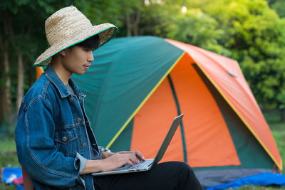 Young man using laptop while sitting by tent