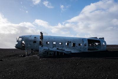 Side view of man standing on abandoned airplane against sky