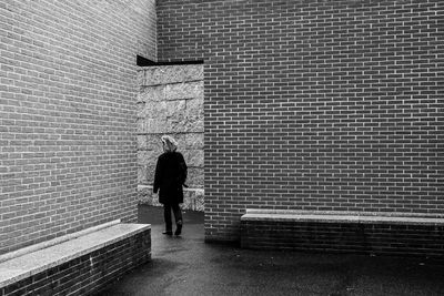 Rear view of man walking on footpath against wall