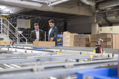 Two businessmen talking at conveyor belt in factory