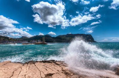 Sea waves splashing on rocks against sky