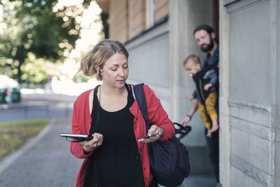 Mid adult woman using mobile phone while leaving for work with family in background