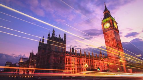 Light trails by illuminated big ben against sky at dusk