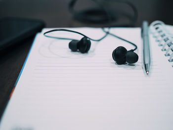 High angle view of in-ear headphones and pen on notebook