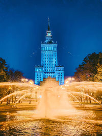 Illuminated buildings against blue sky at night