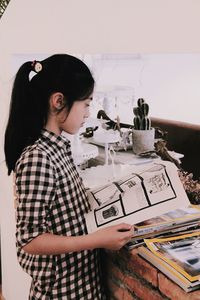 Side view of girl reading book while standing at home