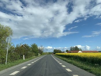 Empty road along trees on field against sky