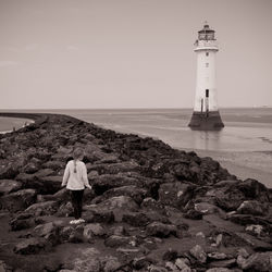 Lighthouse on beach by sea against sky