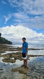 Full length of man standing on rock at beach against sky