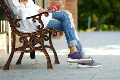 Low section of woman sitting on seat in footpath