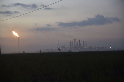 Fire emitting from smoke stack at industrial site against sky