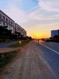 Road by buildings against sky during sunset in city