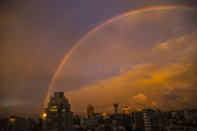 Rainbow over buildings in city against sky during sunset