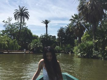 Portrait of young woman by palm trees against sky