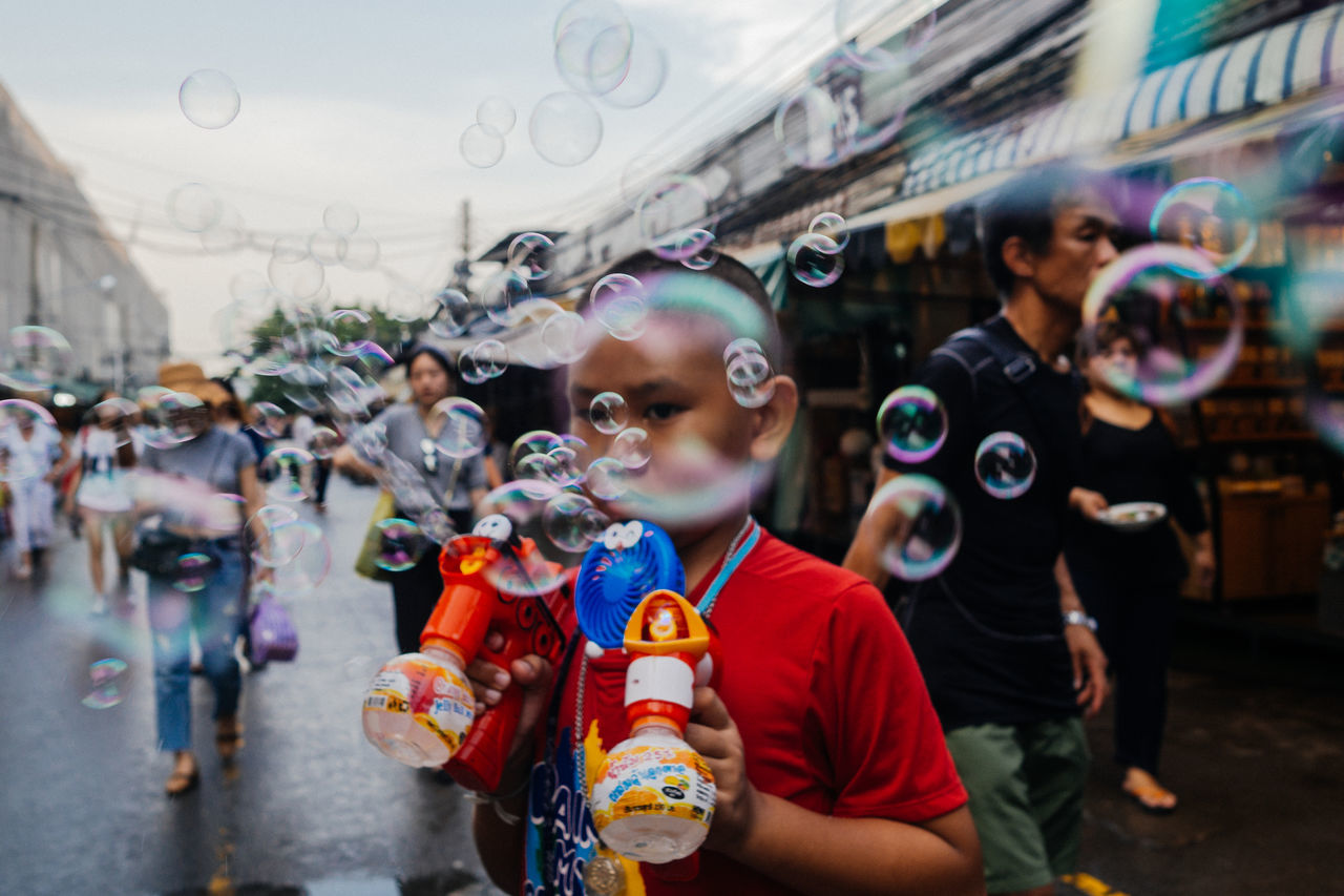 real people, lifestyles, men, childhood, bubble, women, child, group of people, incidental people, leisure activity, people, males, boys, focus on foreground, adult, city, females, casual clothing, girls, innocence