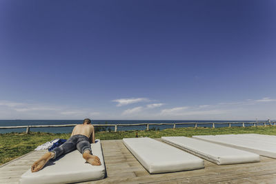 Man lying on mattress against sea and sky