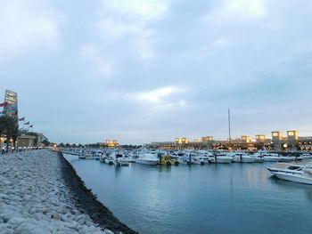 Boats in harbor against cloudy sky