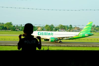 Rear view of man on airport runway against sky