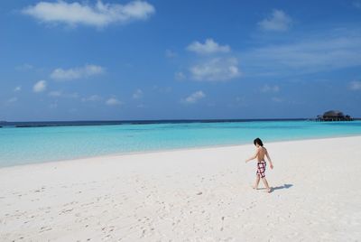Full length of shirtless boy walking on beach against sky
