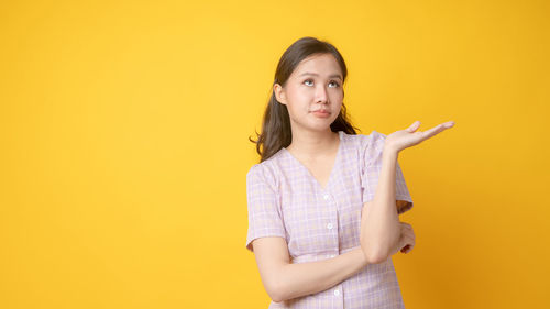 Portrait of beautiful young woman standing against yellow background