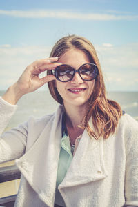 Portrait of smiling young woman wearing sunglasses against sky