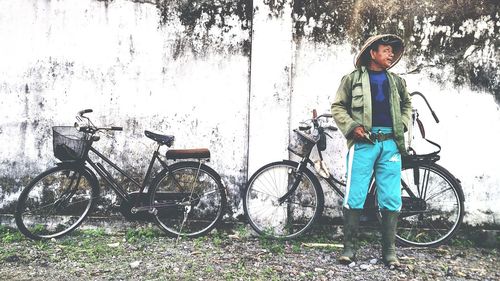 Full length portrait of young woman with bicycle standing against graffiti