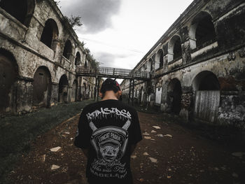 Rear view of man standing by building against sky