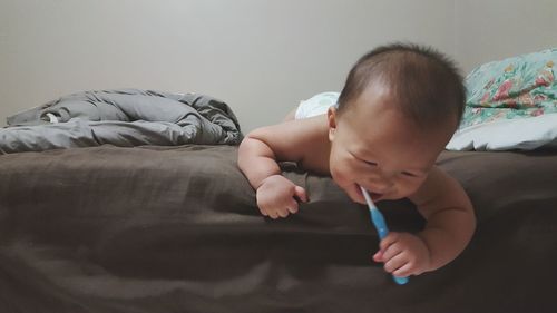 Cute baby boy with toothbrush lying on bed at home