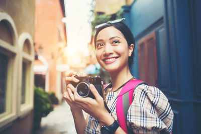 Young woman holding camera standing against building in city