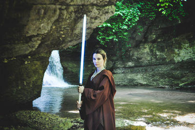 Portrait of woman holding sword standing by water