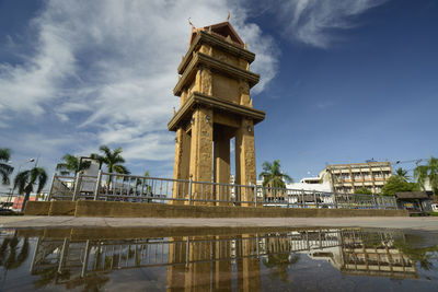 Low angle view of clock tower against sky with reflection on puddle in city