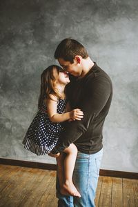 Side view of happy father holding girl while standing on hardwood floor