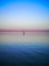 Rear view of woman swimming in sea against sky during sunset