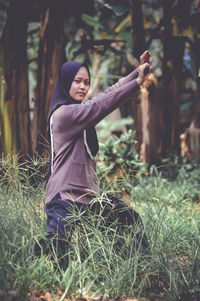 Side view of woman with arms raised standing on field