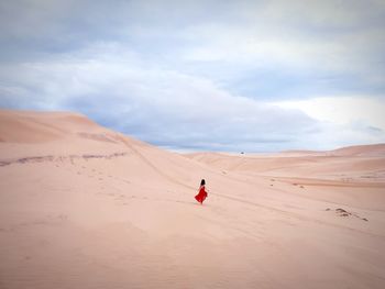 Young woman walking on sand at desert against cloudy sky