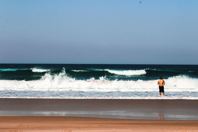 Rear view of shirtless man standing on shore at beach against sky