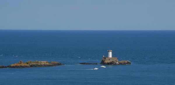 Lighthouse by sea against clear blue sky