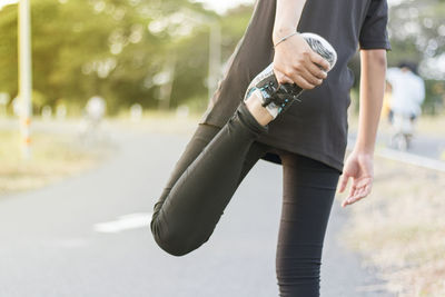 Low section of woman stretching leg while standing on road in city