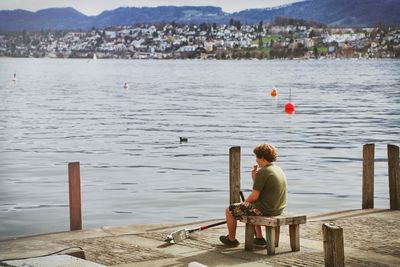 Rear view of boy sitting on stool at pier