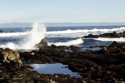Waves splashing on rocks at shore against sky