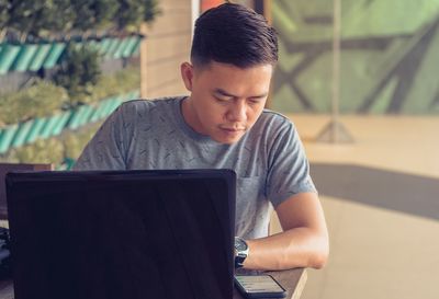 Mid adult man checking phone while using laptop on table at home