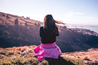 Rear view of woman sitting on mountain peak against sky