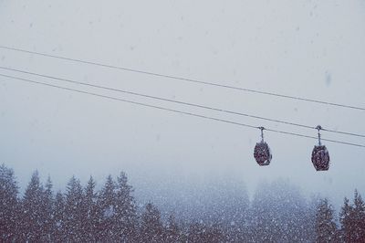 Low angle view of ski lift against sky during snowfall