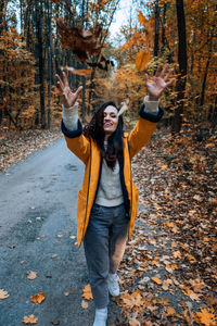 Happy brunette woman holding yellow maple autumn leaves in fall park.