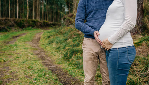 Midsection of pregnant couple touching abdomen while standing on grass 