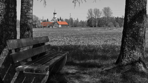 Abandoned bench on field by buildings against sky