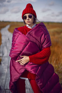 Woman  in red warm clothes and a big scarf on an ecological trail in the autumn not a swamp