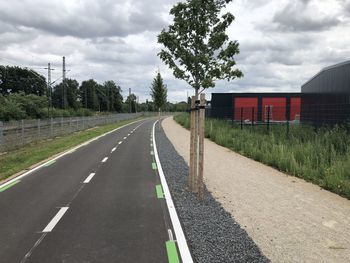 Empty road by trees against sky