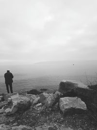 Rear view of man standing on rock by sea against sky