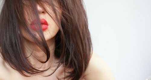 Close-up of beautiful young woman face covered with hair against white background